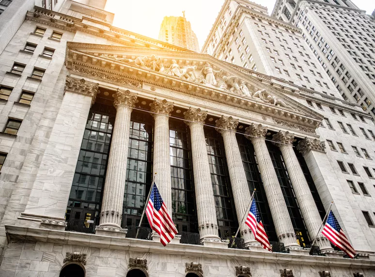 New York Stock Exchange building with American flags and surrounding skyscrapers. New York Stock Exchange building with American flags and surrounding skyscrapers.