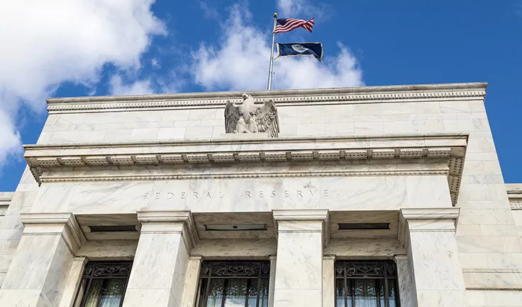 Federal Reserve building facade with U.S. flags against a blue sky. Federal Reserve building facade with U.S. flags against a blue sky.